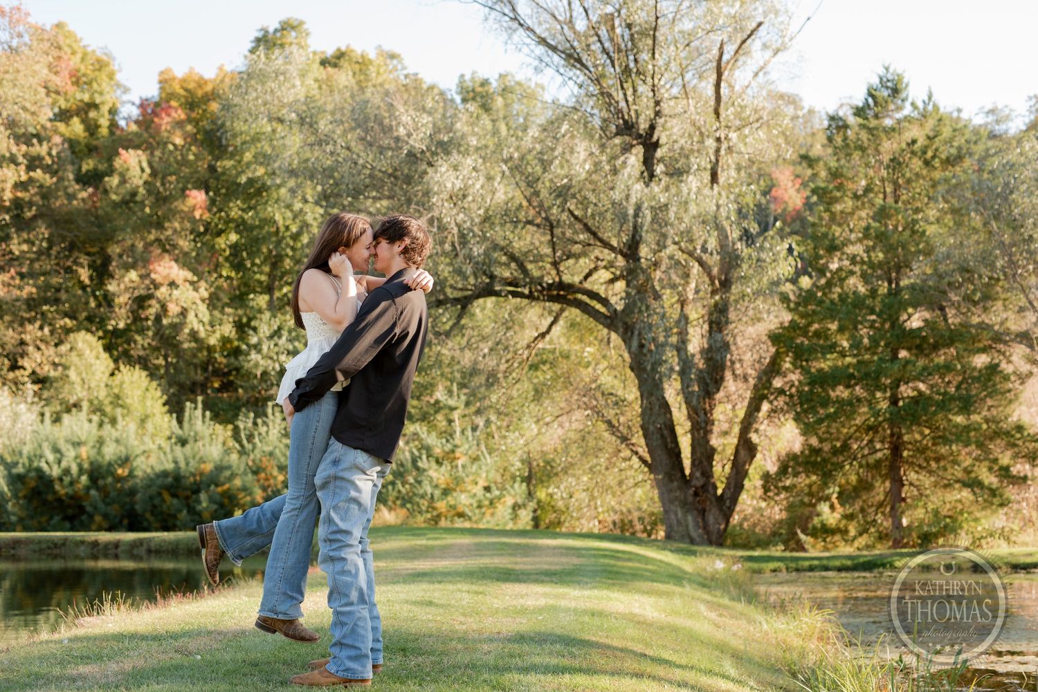 A couple embraces in front of an autumn pond landscape during golden hour.