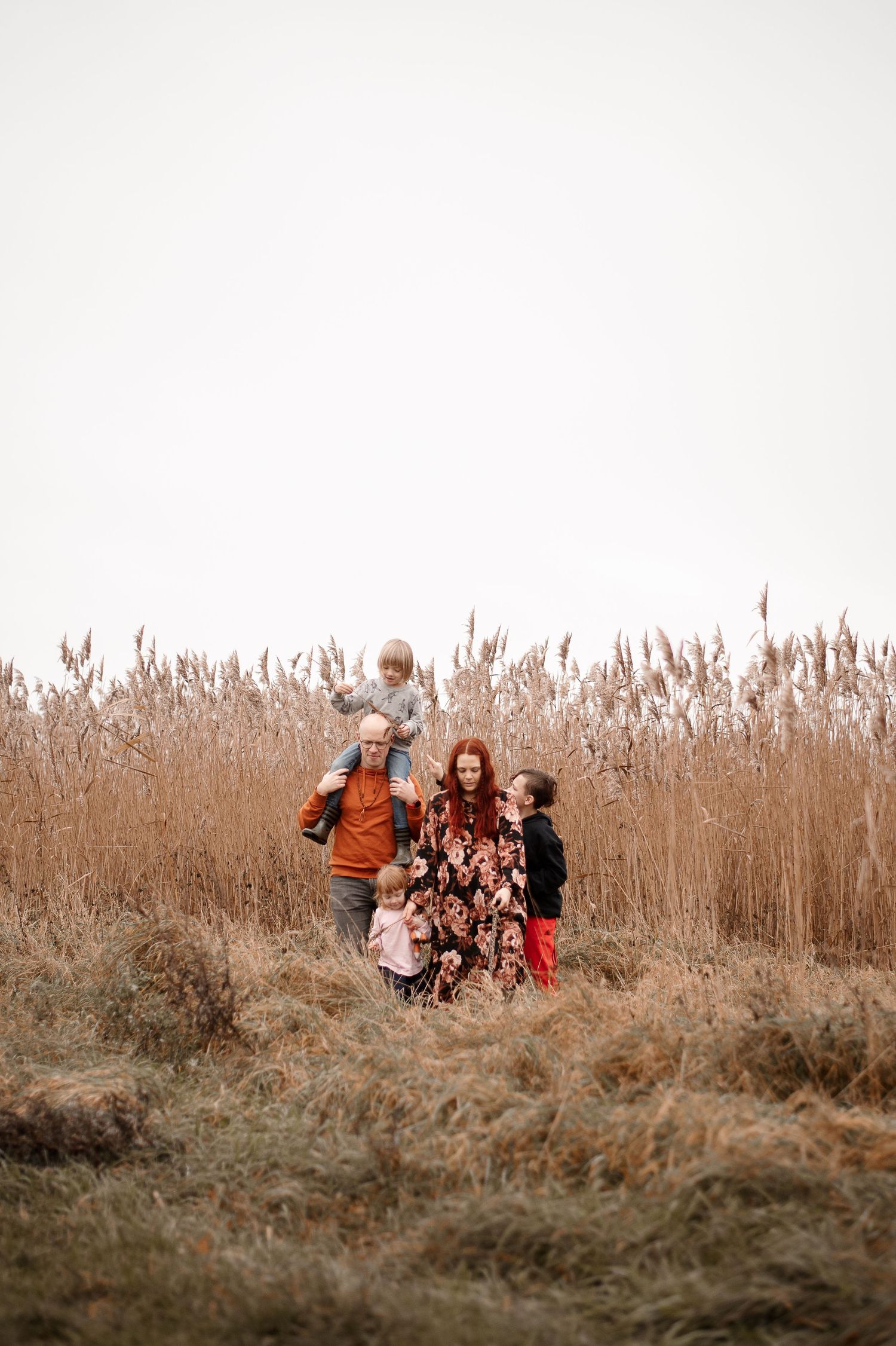 Family group standing in tall sepia-toned grass field during golden hour.