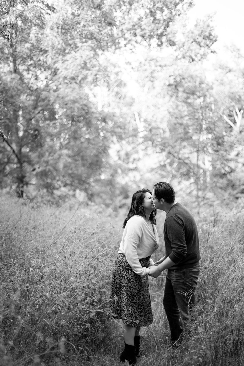 A romantic black and white portrait of a couple embracing in a misty field.