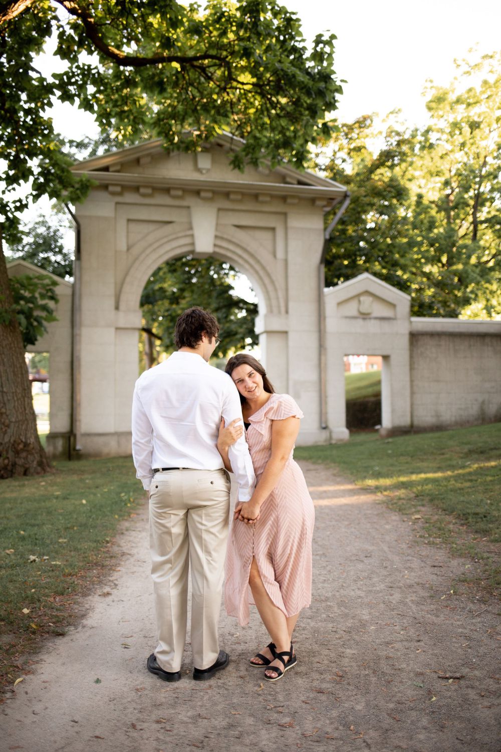 A couple in light-colored outfits shares a tender moment by a stone archway entrance.