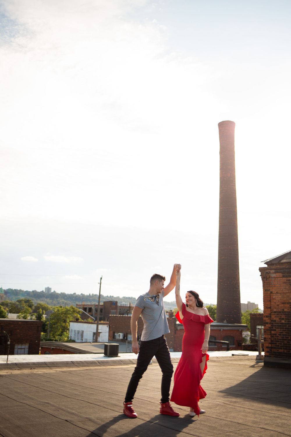 A couple dances together on a rooftop terrace with a tall industrial chimney in the background.