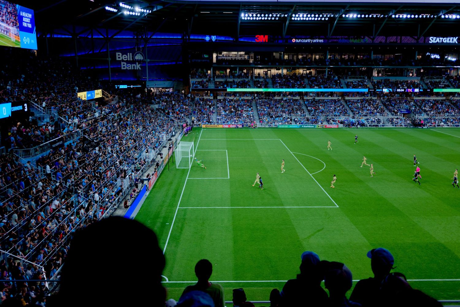 Wide angle view of packed soccer stadium at night with players on illuminated green field.