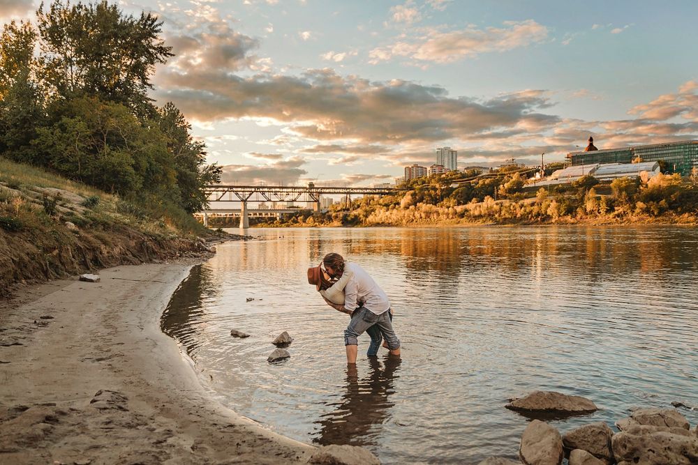 A sunset moment by a riverside with seagulls and a cityscape in the background.