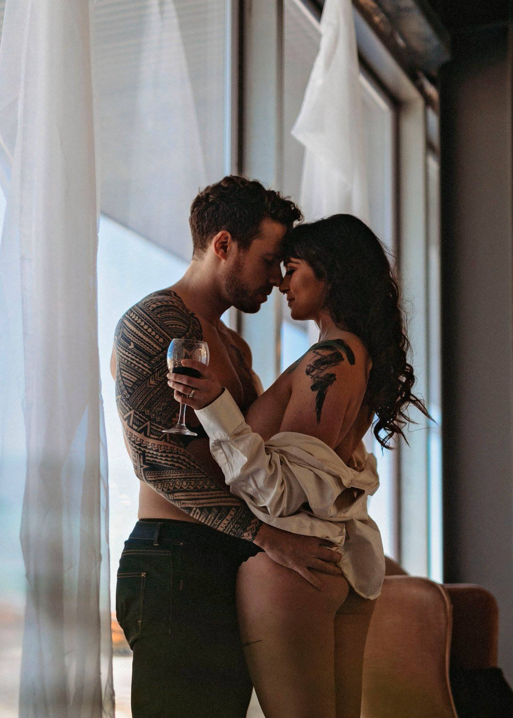 Intimate couple sharing romantic moment by window with wine glass.