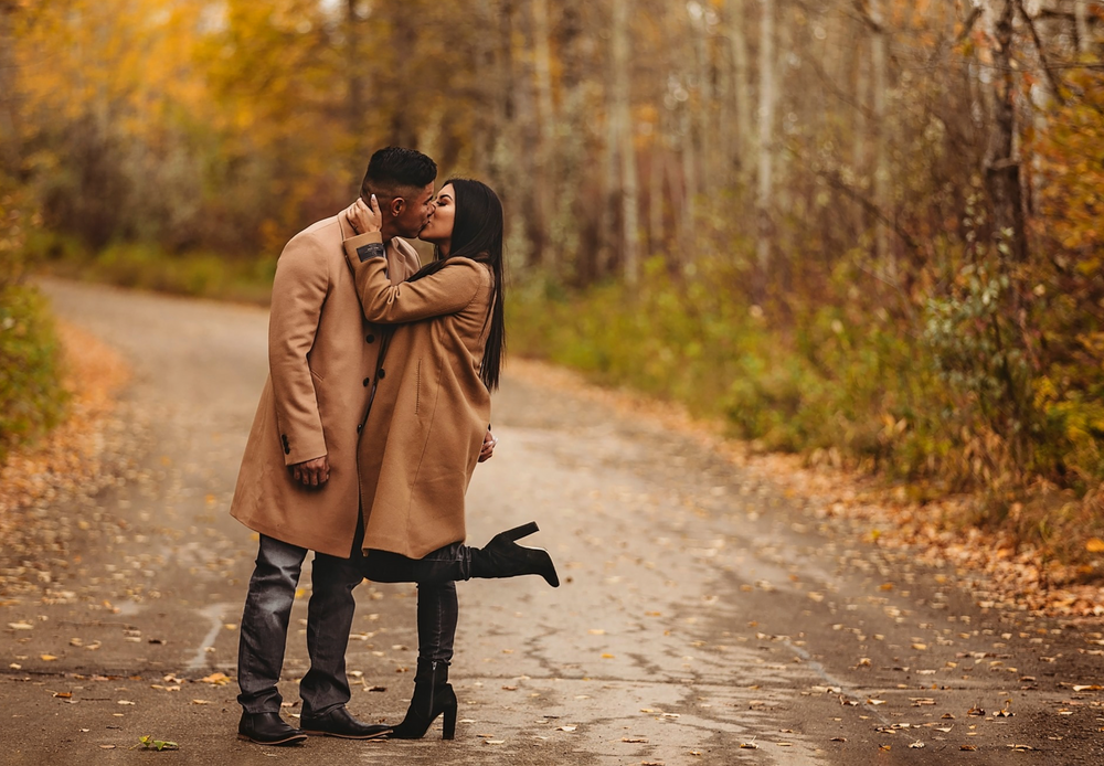 A romantic couple embraces on a fall path surrounded by golden leaves and trees.
