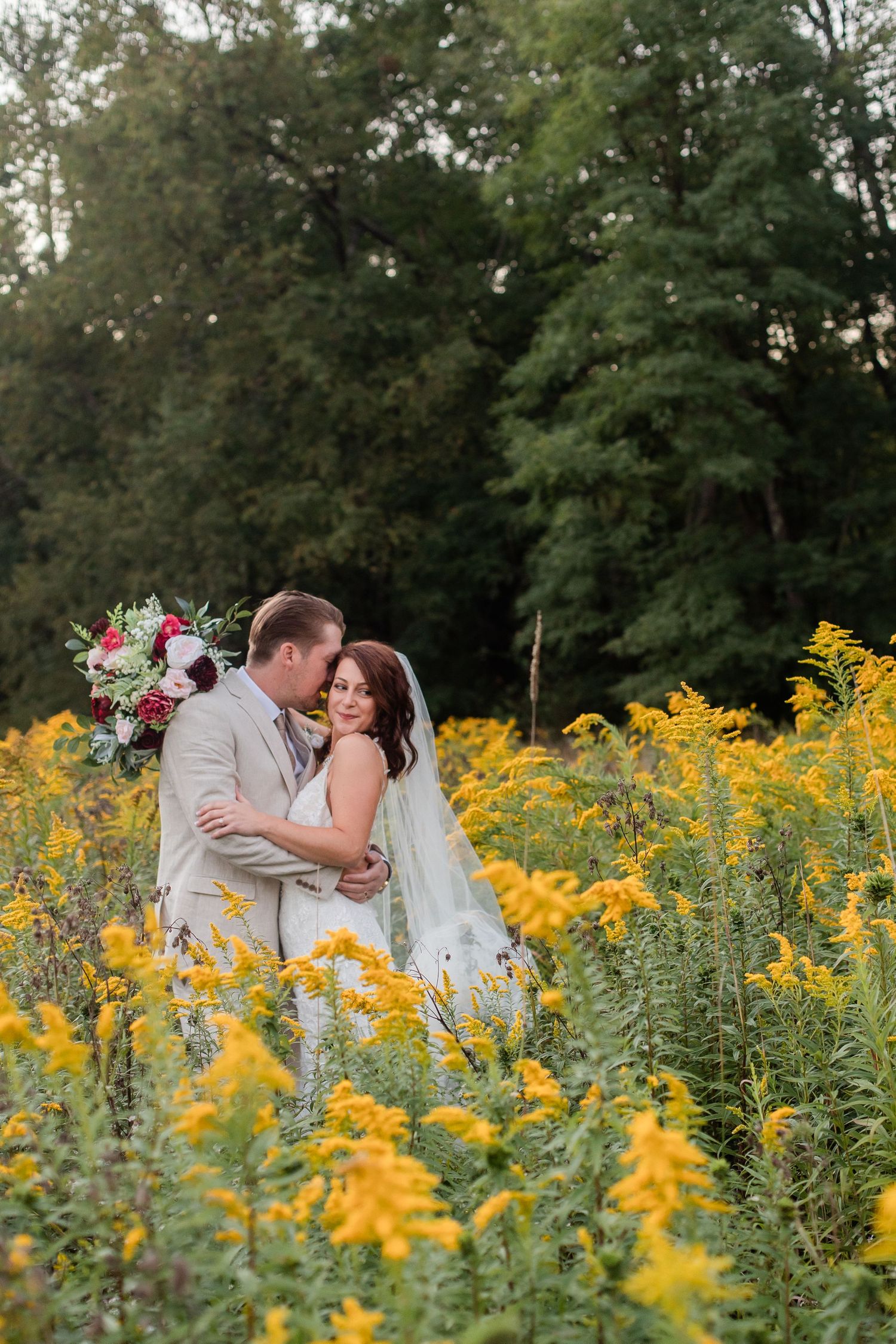Couple shares intimate moment surrounded by blooming yellow goldenrod flowers in garden setting.