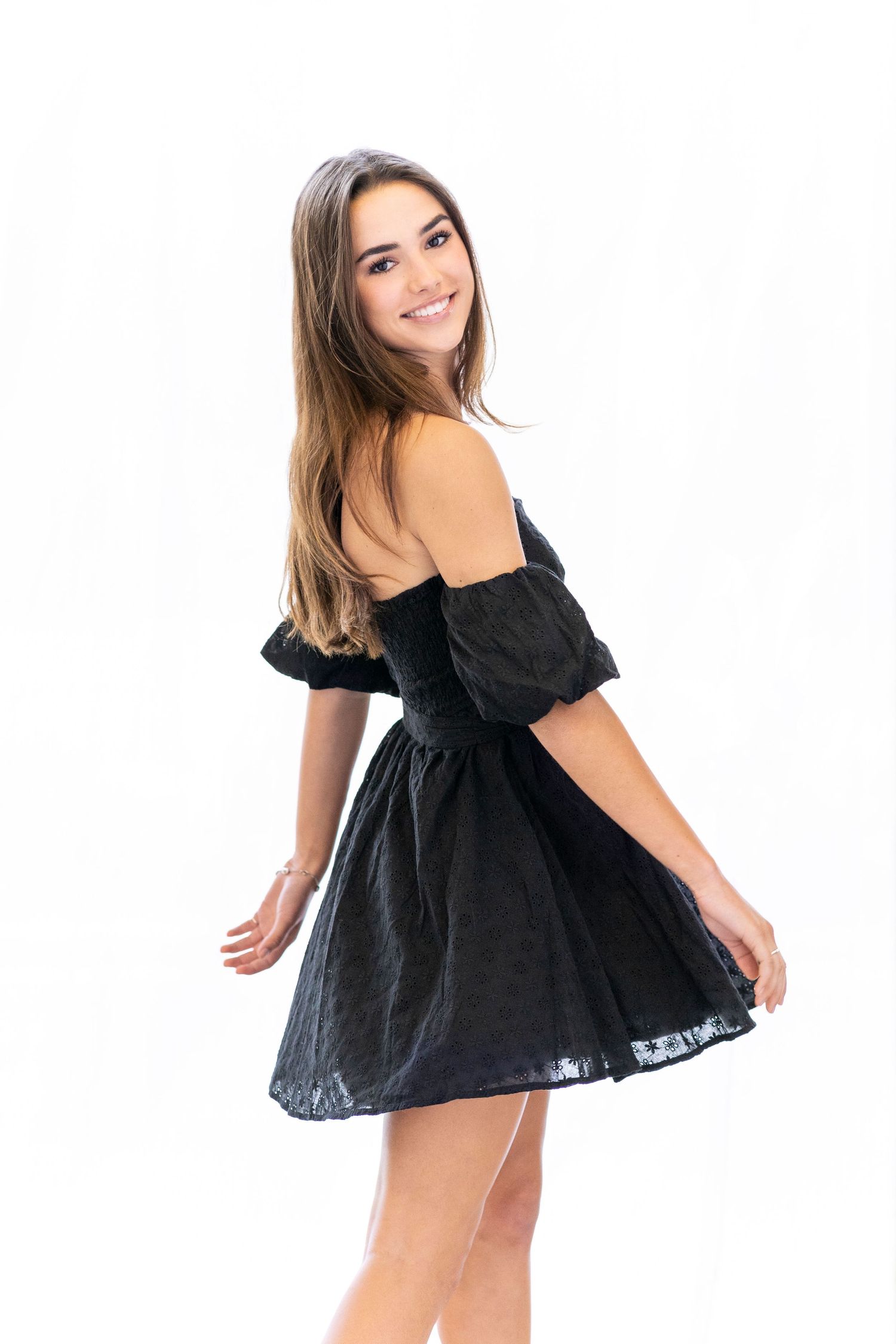 Woman in black off-shoulder dress twirling against white background.
