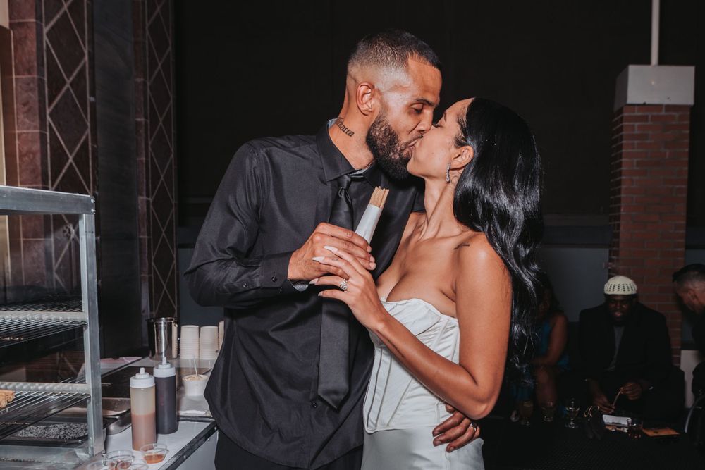 A couple in formal attire share an intimate moment while holding drinks at an evening reception.