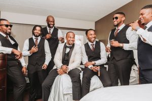 Groomsmen in matching black vests and white shirts share a candid moment during wedding preparations.