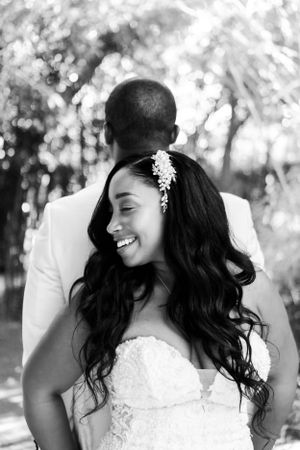 Black and white wedding photo showing couple in sweet candid moment outdoors with bride wearing floral hairpiece.
