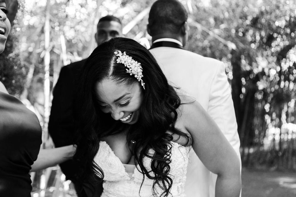 A joyful bride laughs during an outdoor wedding celebration, wearing a white dress and delicate hair accessory.