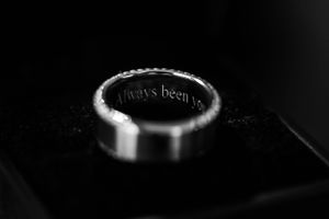 A close-up black and white macro photograph of an engraved metal bottle cap on a dark background.
