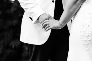 Black and white closeup of joined hands with wedding rings at a marriage ceremony.