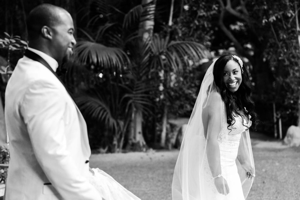Black and white photo of a wedding couple in a garden setting with palm trees, bride wearing long veil.