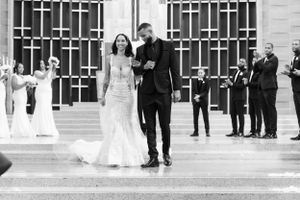 A black and white wedding photo showing a couple exiting a building while guests celebrate with bubbles in the background.