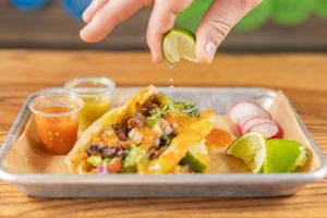 Close-up of hands garnishing tacos with lime and fresh toppings.