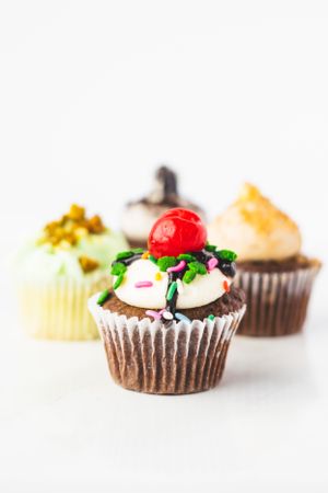 Row of decorated chocolate cupcakes with various colorful toppings on white background.