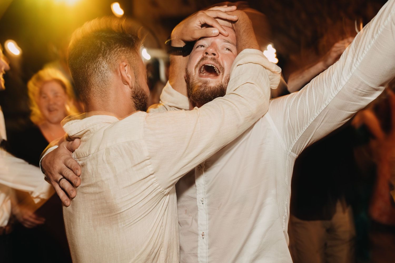 Wedding guests embrace joyfully during lively dance celebration.