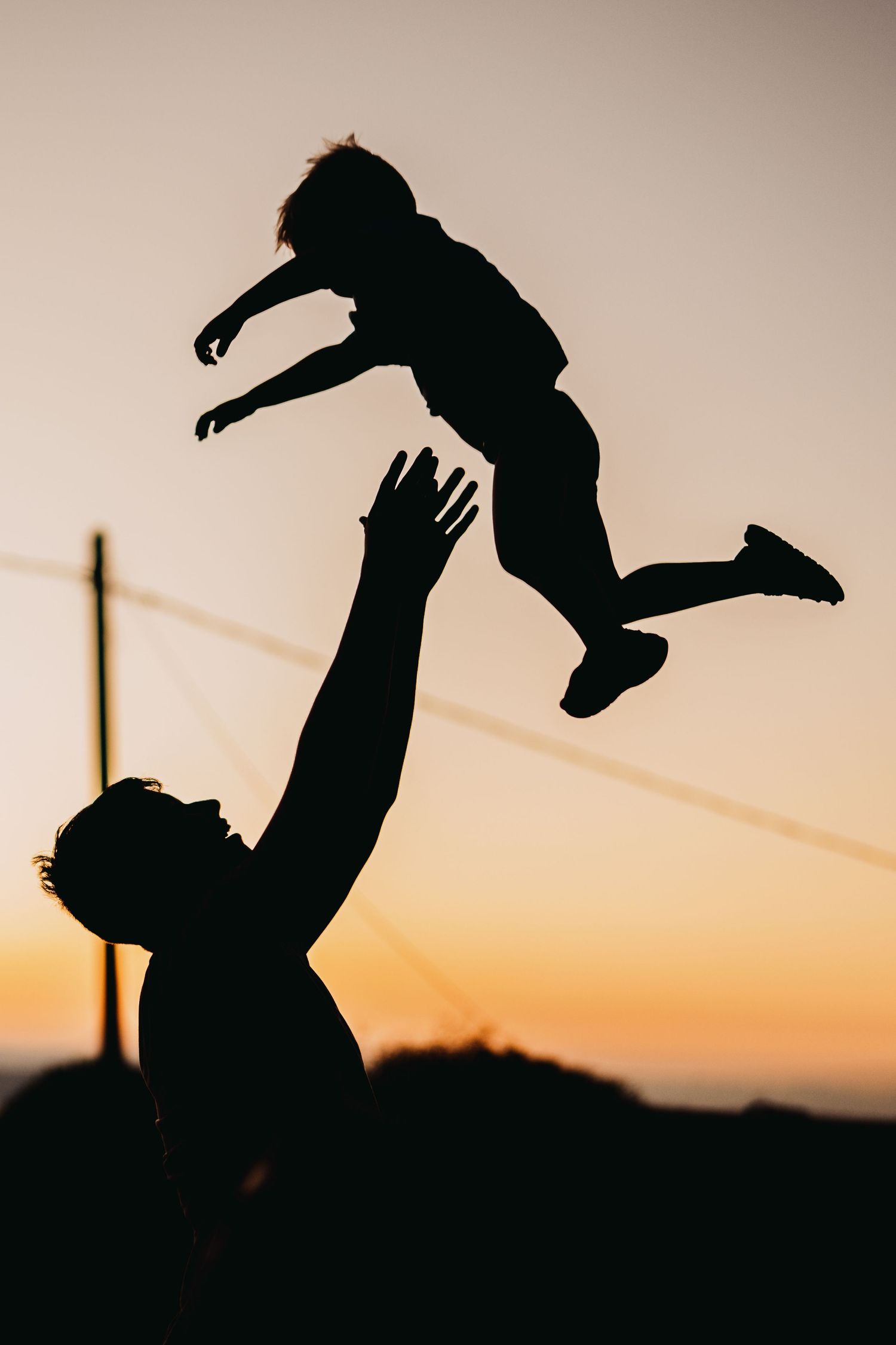 Silhouette of parent tossing child in air against sunset sky.