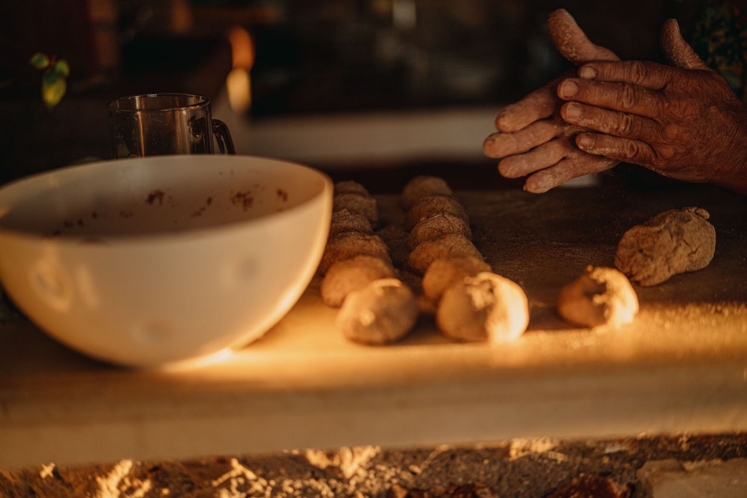 Fresh bread dough being prepared on a wooden surface with a mixing bowl in warm lighting.