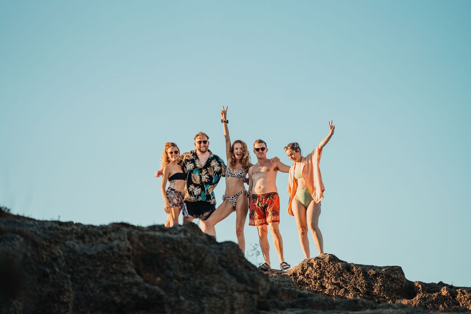 Friends posing triumphantly on rocky cliff against blue sky backdrop.