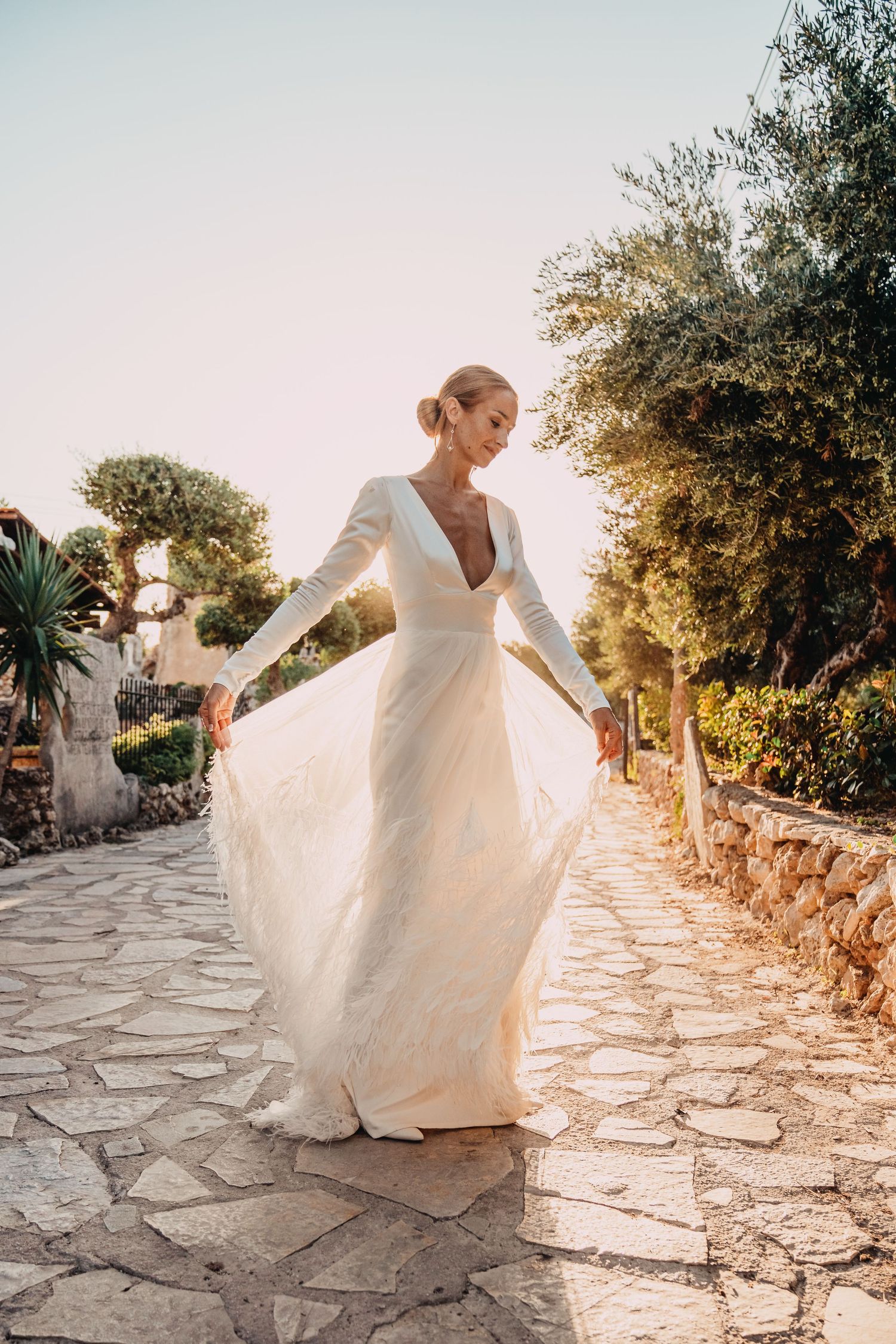 A flowing white wedding gown twirls on a Mediterranean stone pathway during golden hour.