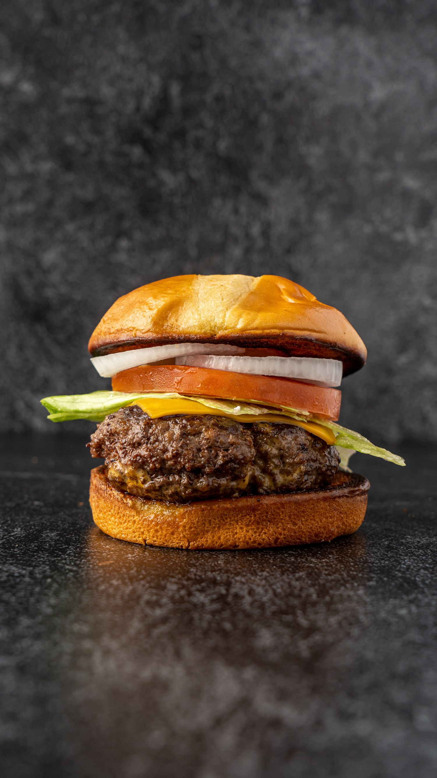 A juicy hamburger with fresh toppings on a brioche bun against a dark background.