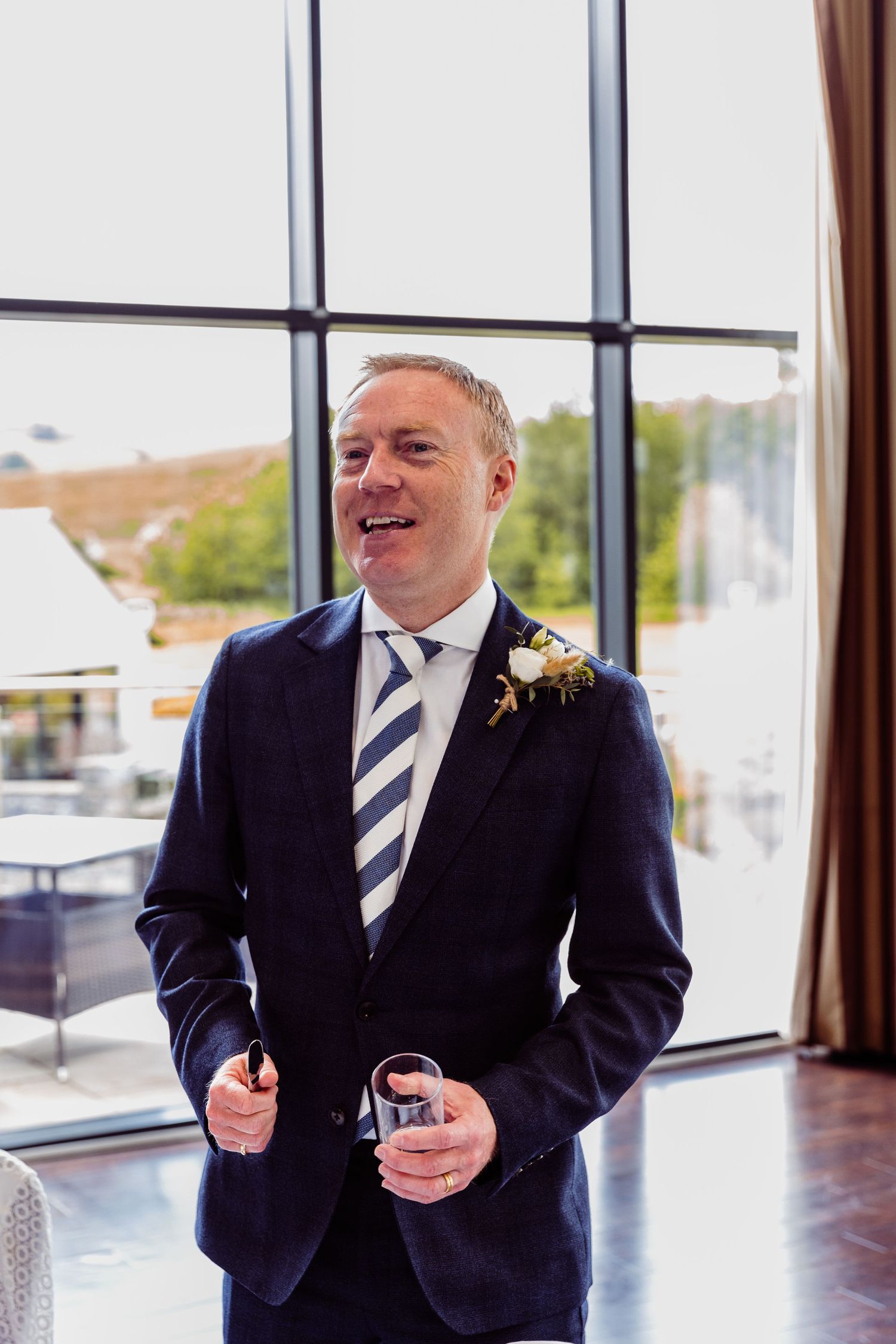 Formal event at modern venue showing well-dressed attendee by large windows.
