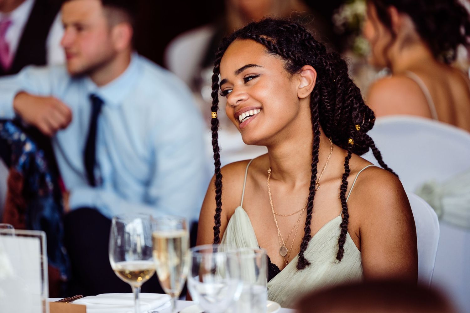 A wedding guest smiles joyfully while seated at an elegant dinner table with wine glasses.