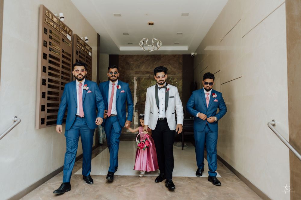 Wedding party in blue suits and white tuxedo pose in hotel hallway.