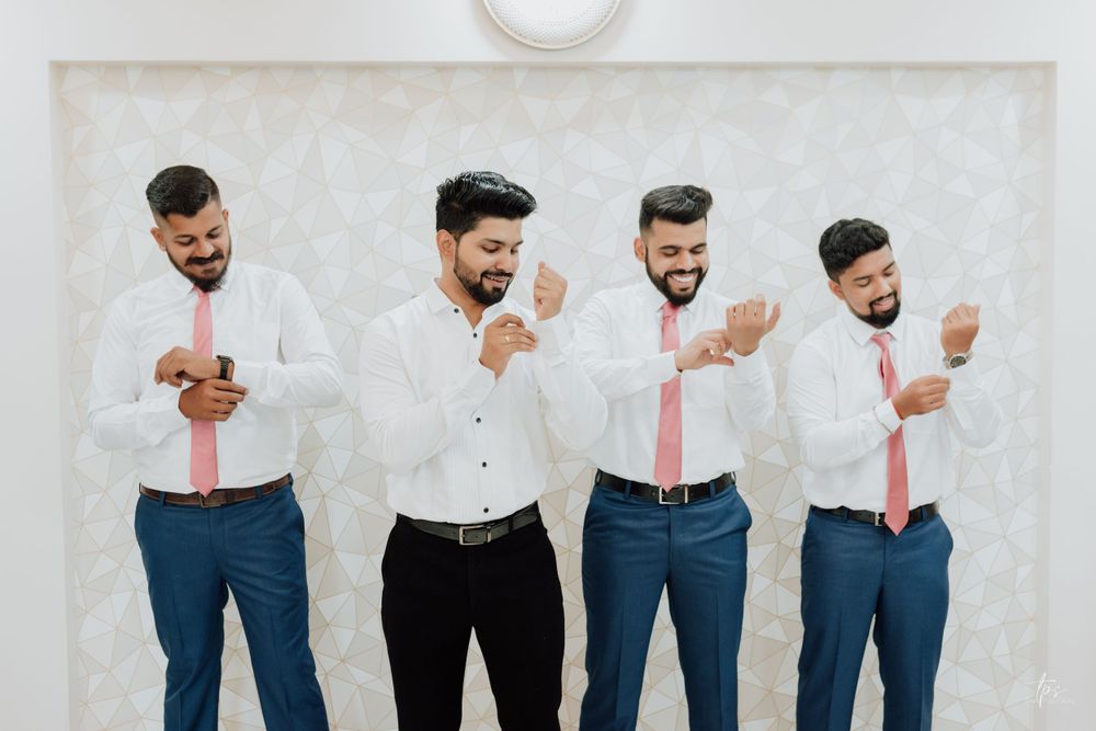 Groomsmen in matching navy pants and white shirts posing against white wall.