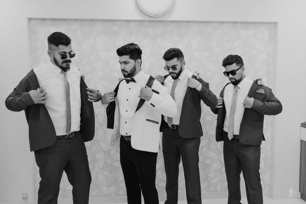 Groomsmen in formal attire pose while putting on their jackets in black and white.