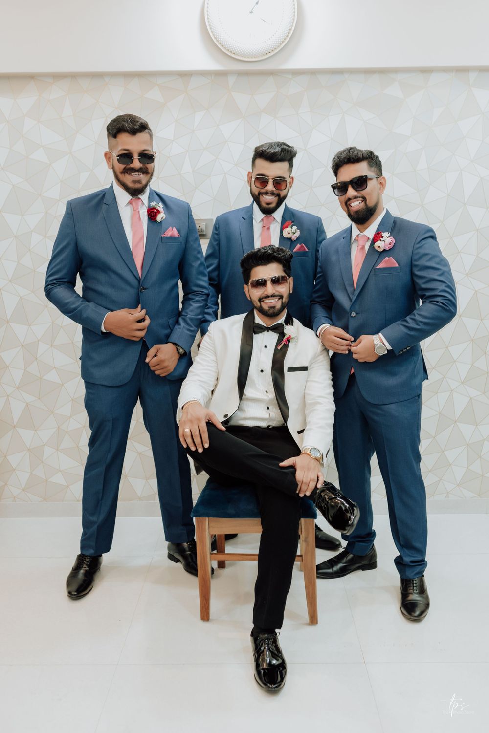 Wedding party in blue suits and sunglasses pose together with one member seated on a wooden chair.