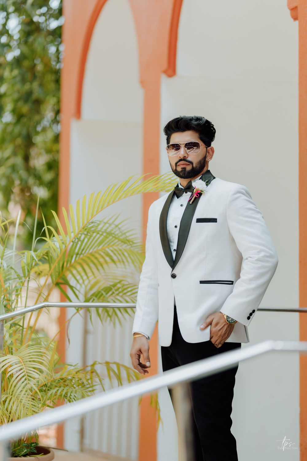 White tuxedo with black lapels photographed against coral archway and tropical foliage.