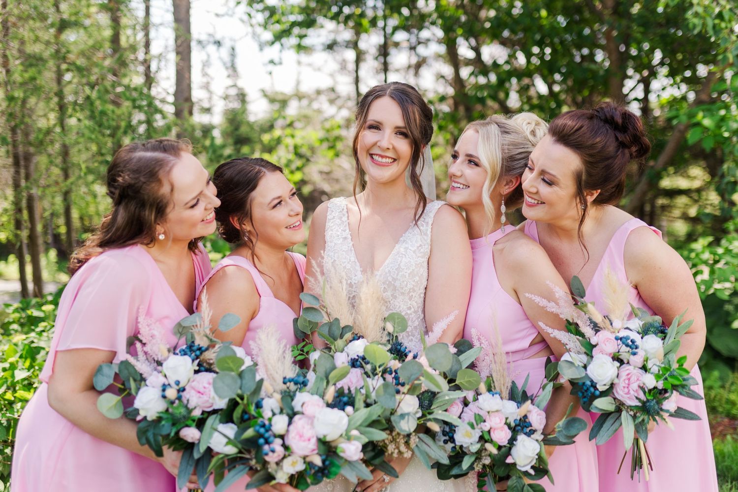 Wedding party members in pink dresses share laughter while holding floral bouquets.