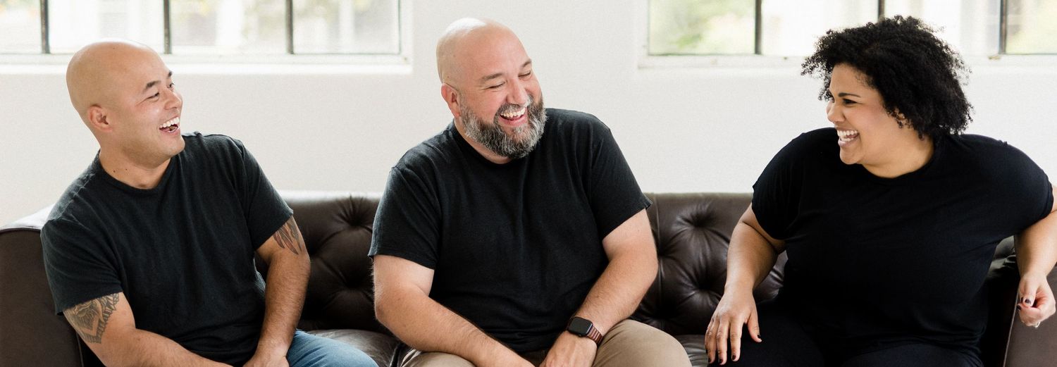Three photographers having animated conversation while sitting together in bright studio.