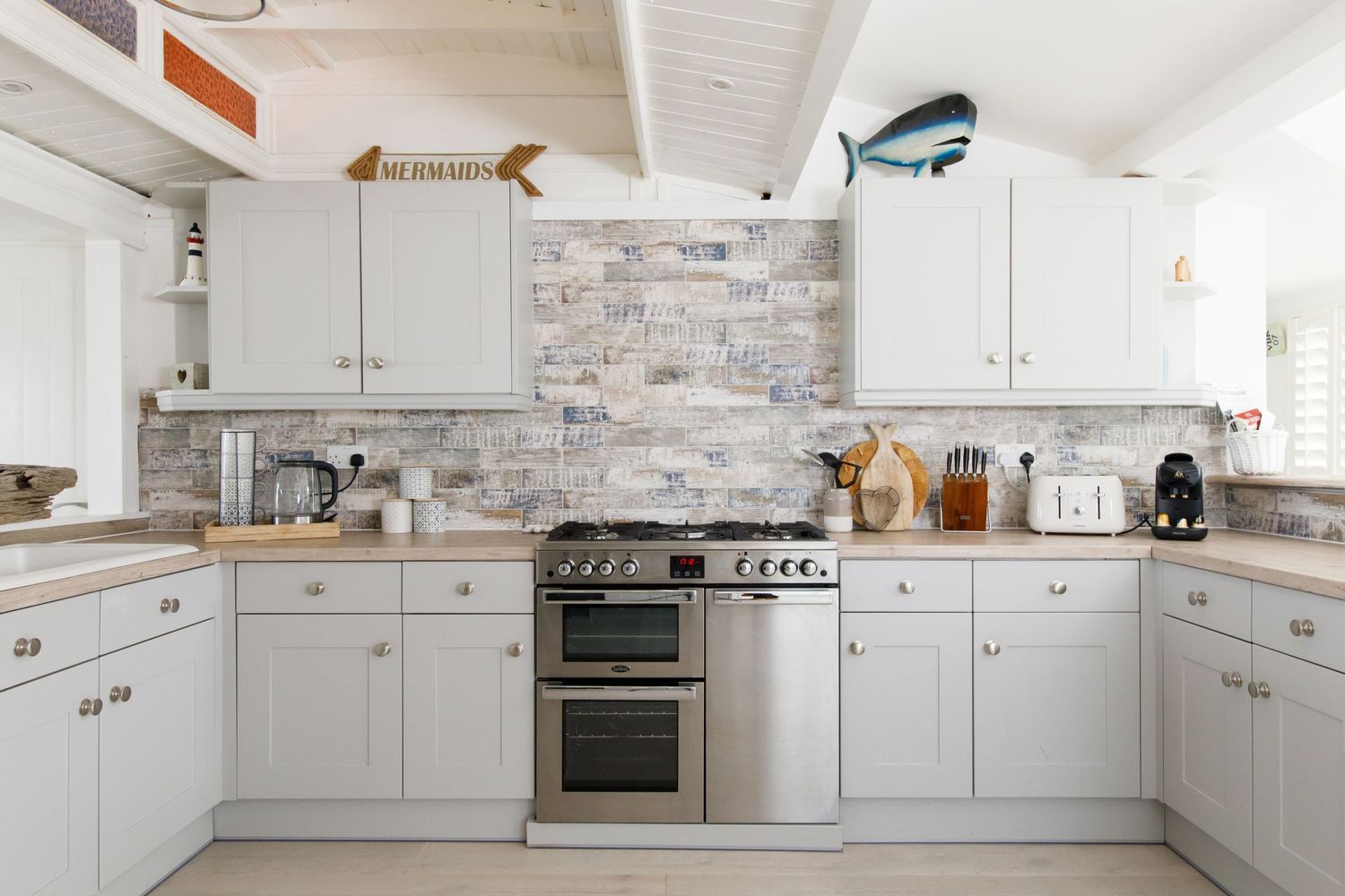 Modern white kitchen with gray stone backsplash, stainless steel appliances, and white cabinets in L-shape layout.