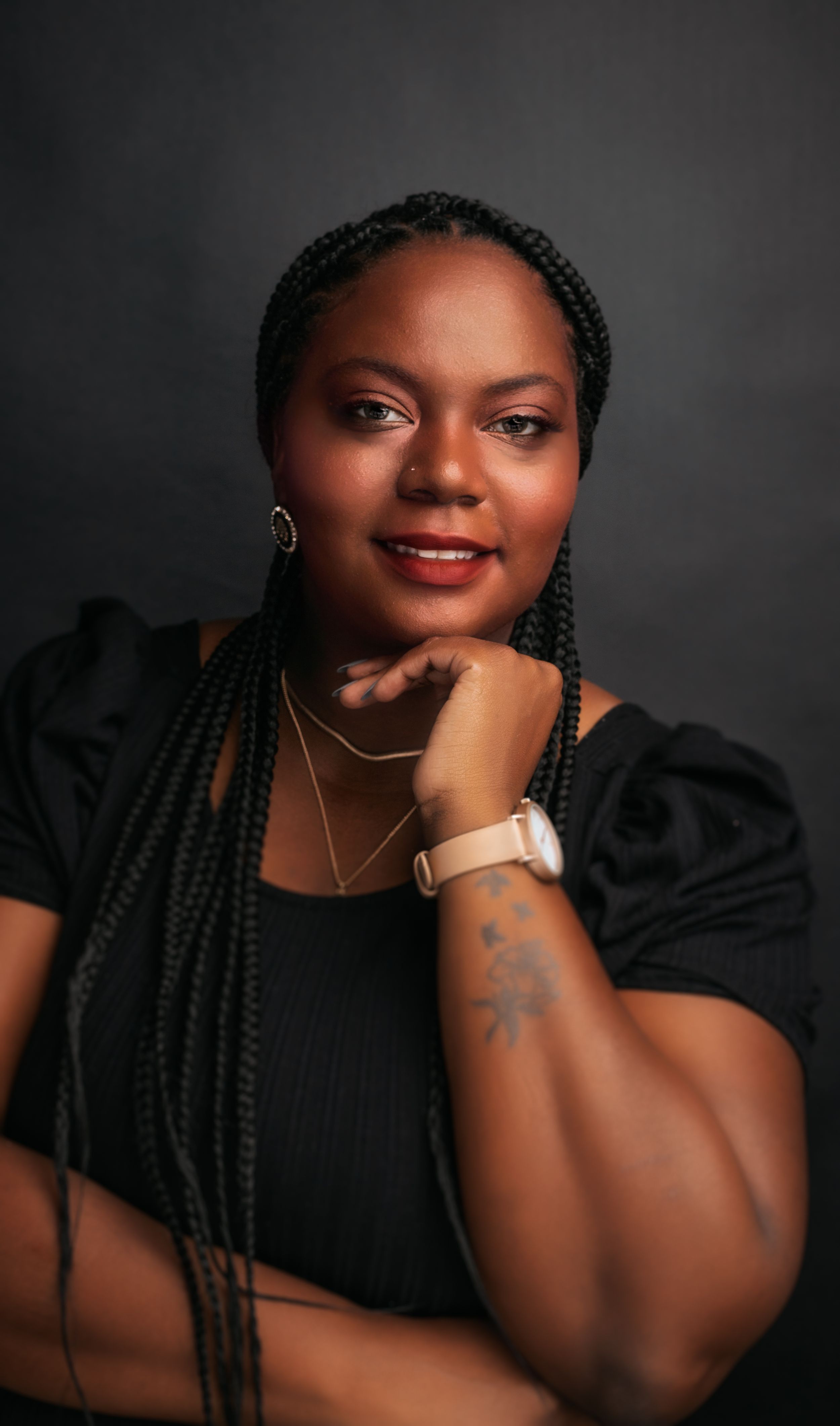 Professional studio portrait with long braids, black puff sleeve top, and elegant jewelry.