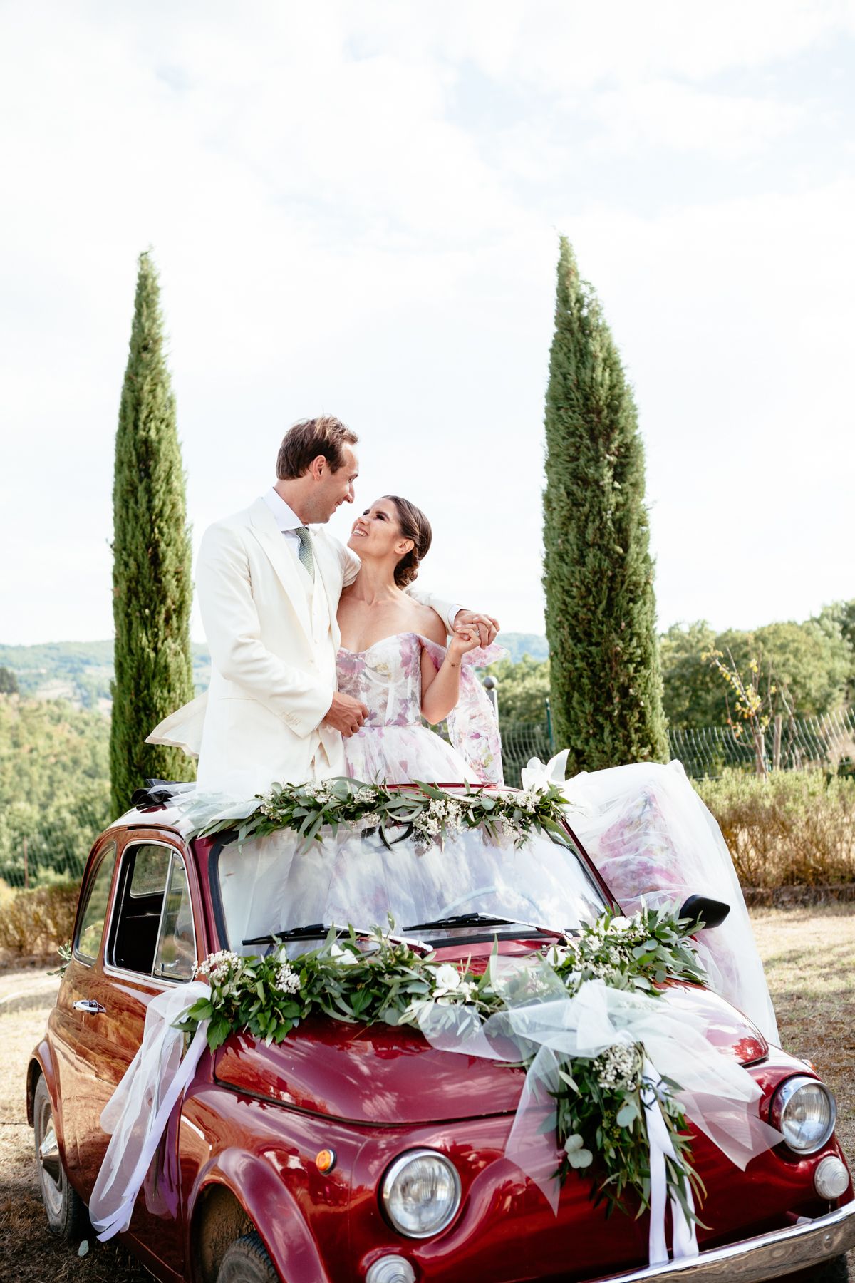 bride and groom stand out the sun roof of a fiat 500 for the wedding in Tuscany