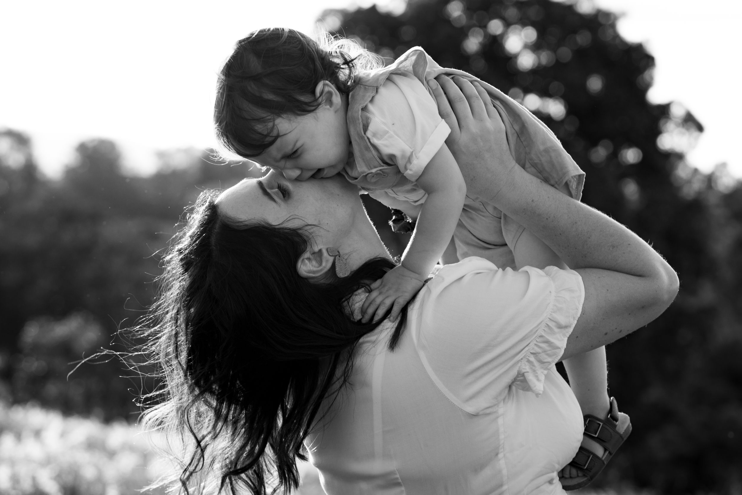 Mother lifts crying toddler in the air, comforting him with a kiss