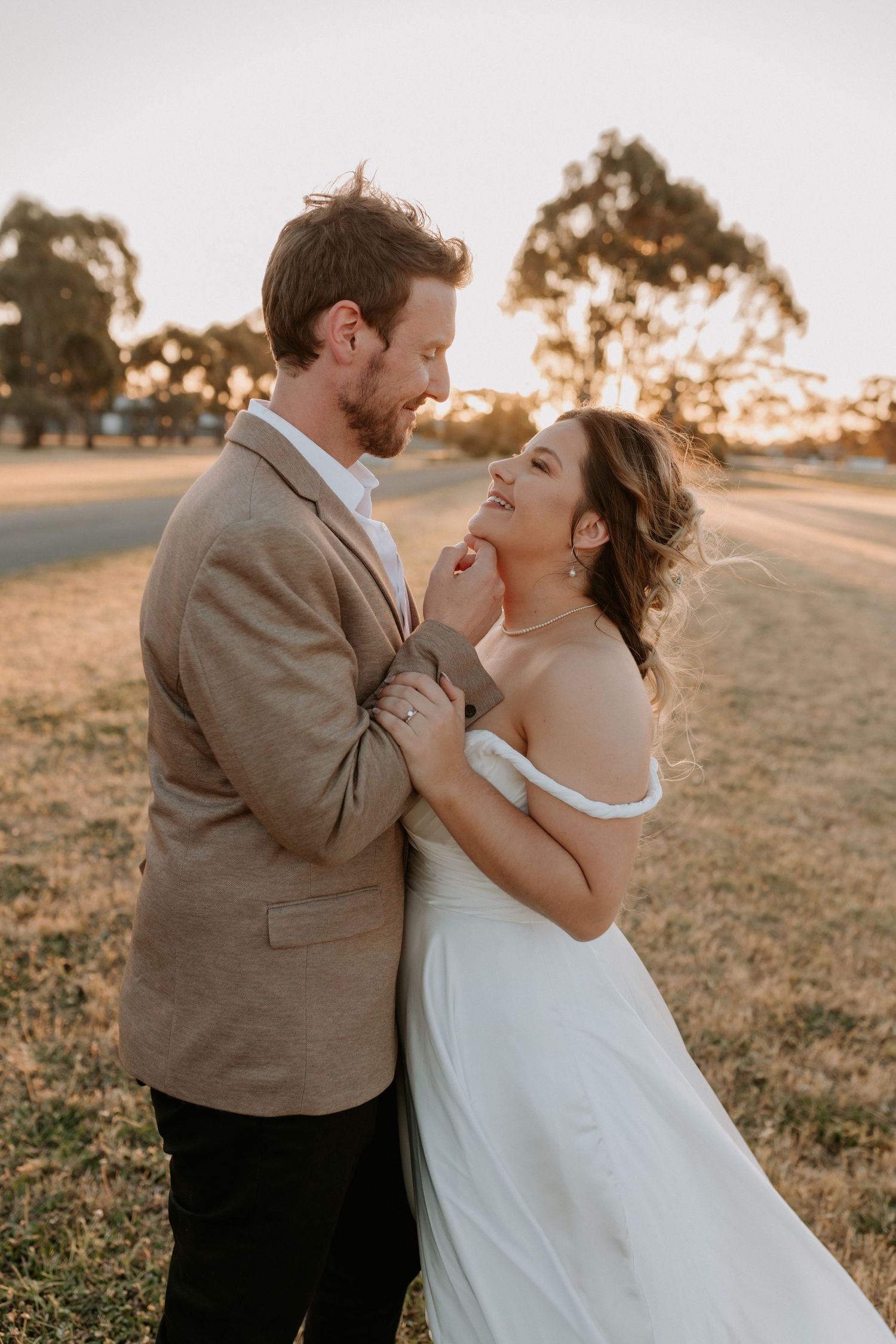 Intimate sunset wedding portrait of couple laughing together in countryside setting.
