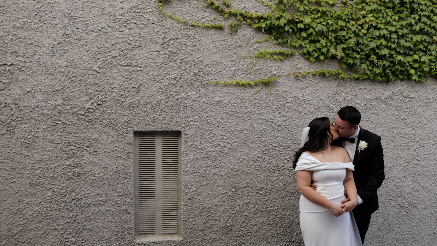 A romantic moment between a couple against a textured gray wall with climbing vines.