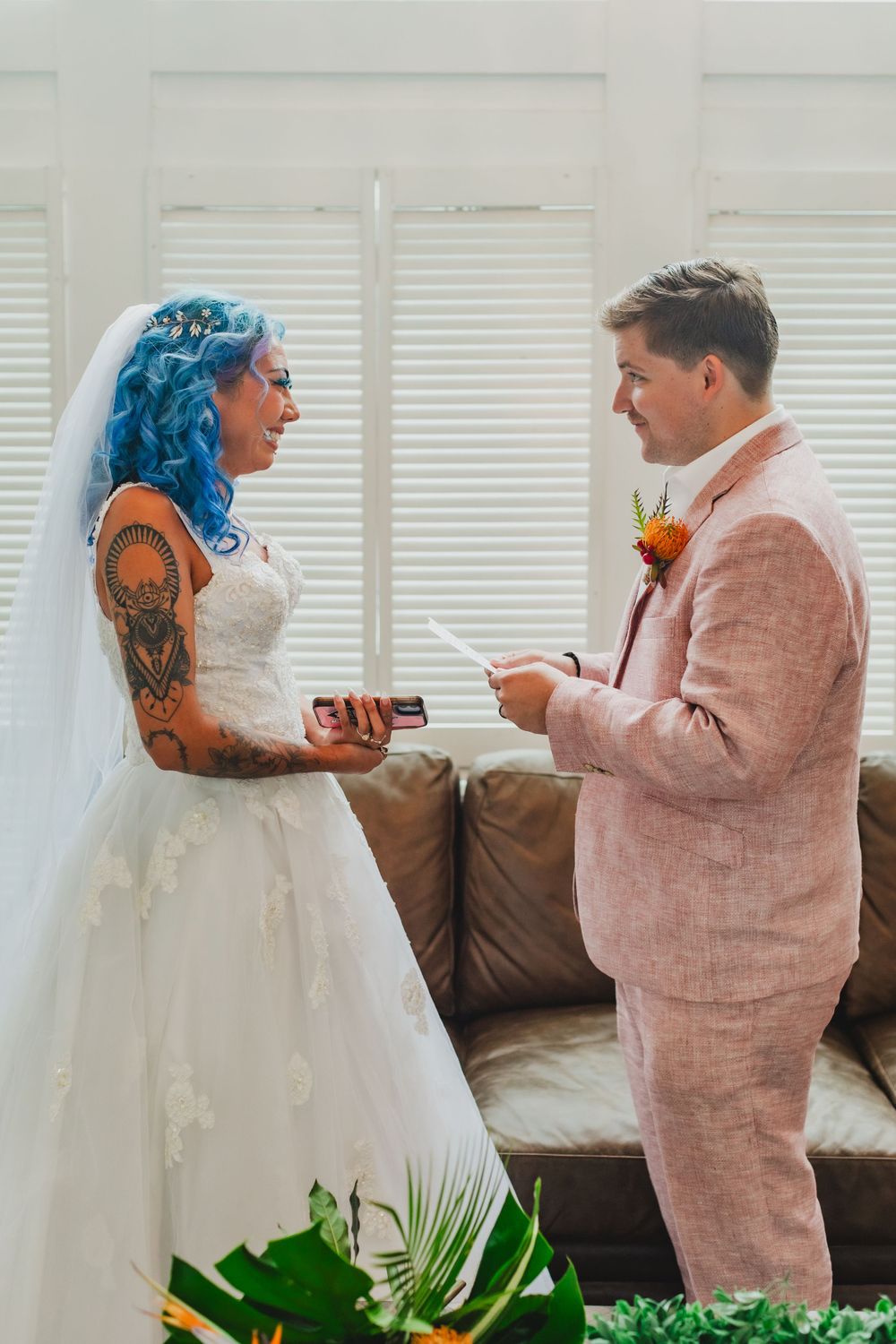 A wedding ceremony moment showing vow exchange in an indoor setting with white decor.