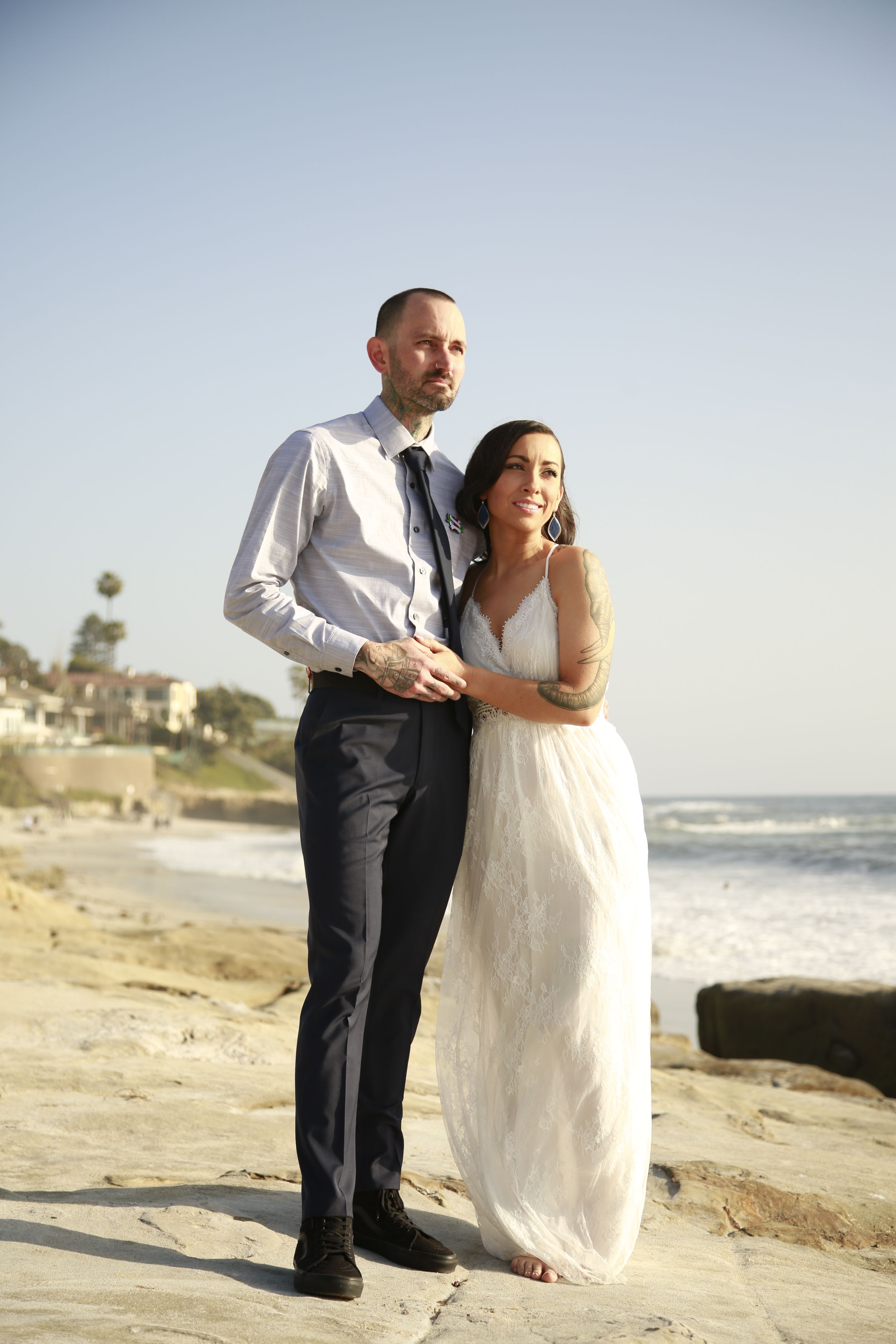Newlyweds pose together on sandy beach with ocean waves in background.