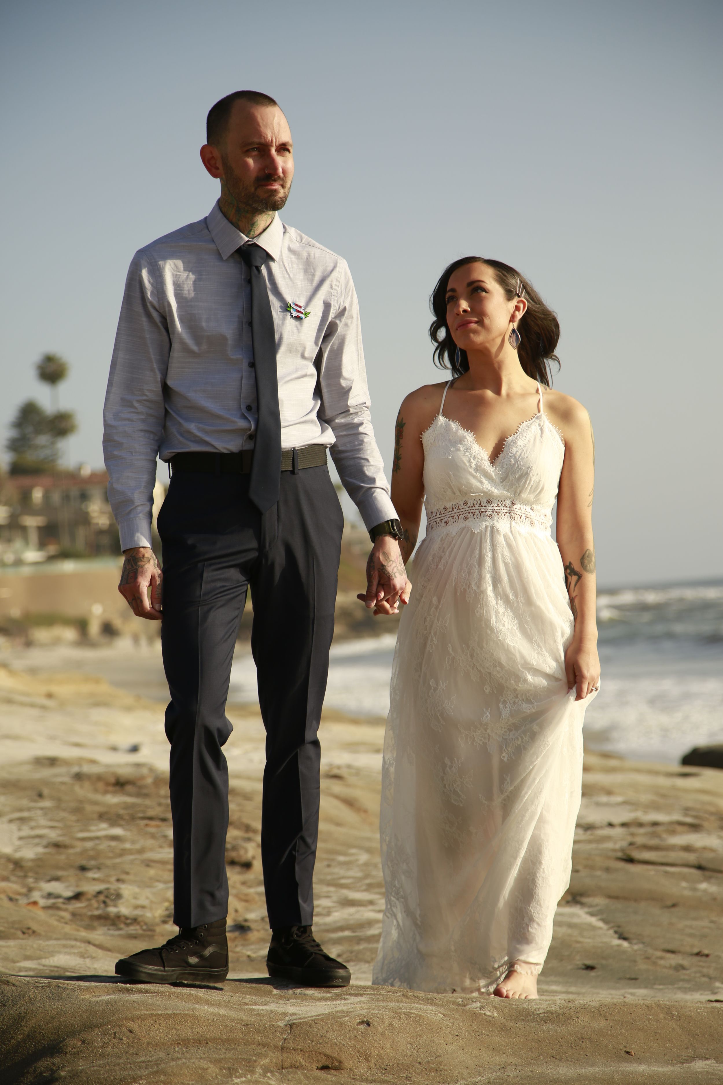 Couple poses for romantic beach wedding photos with coastal backdrop.