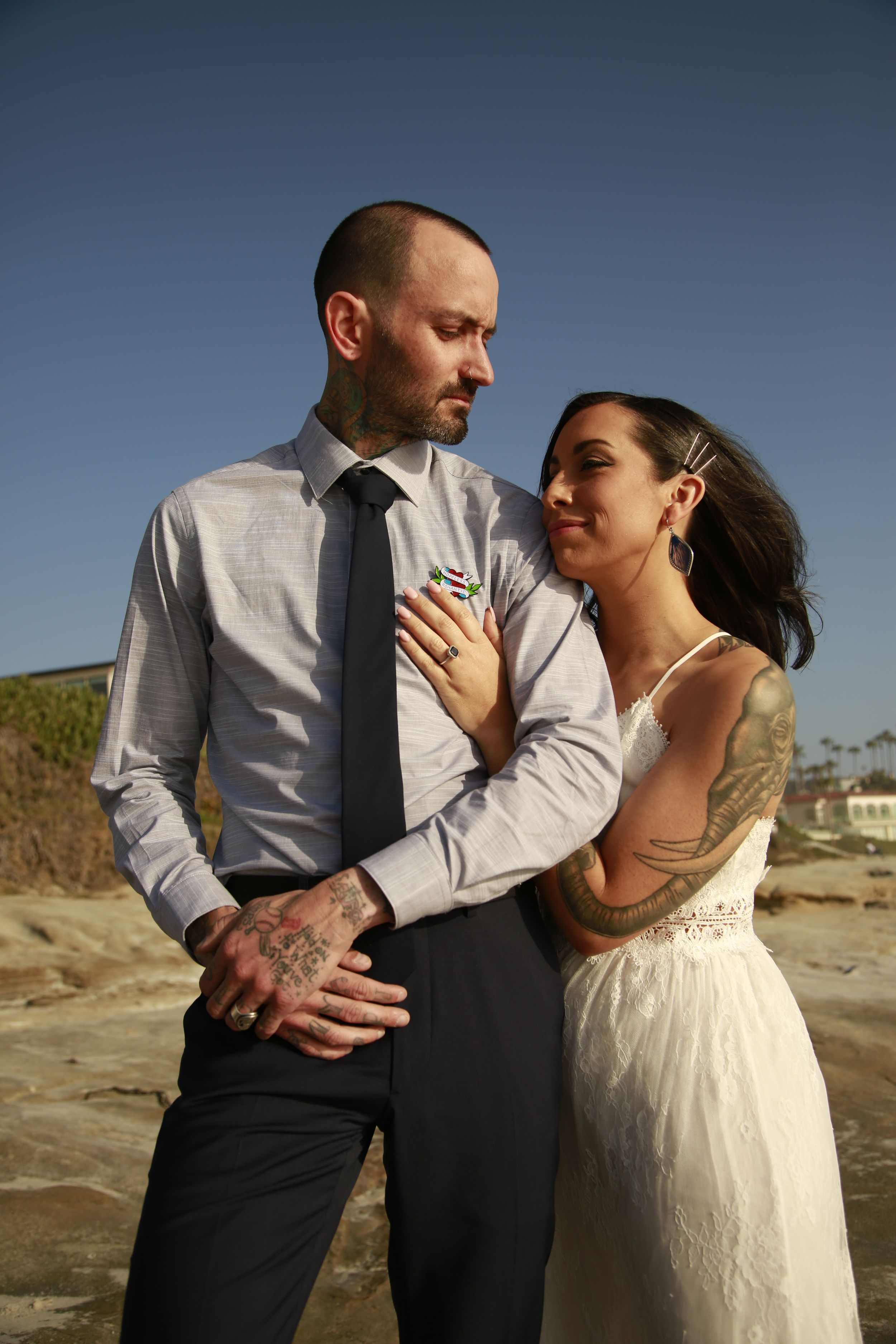 A tender moment between newlyweds on a beach with cliffs in the background.