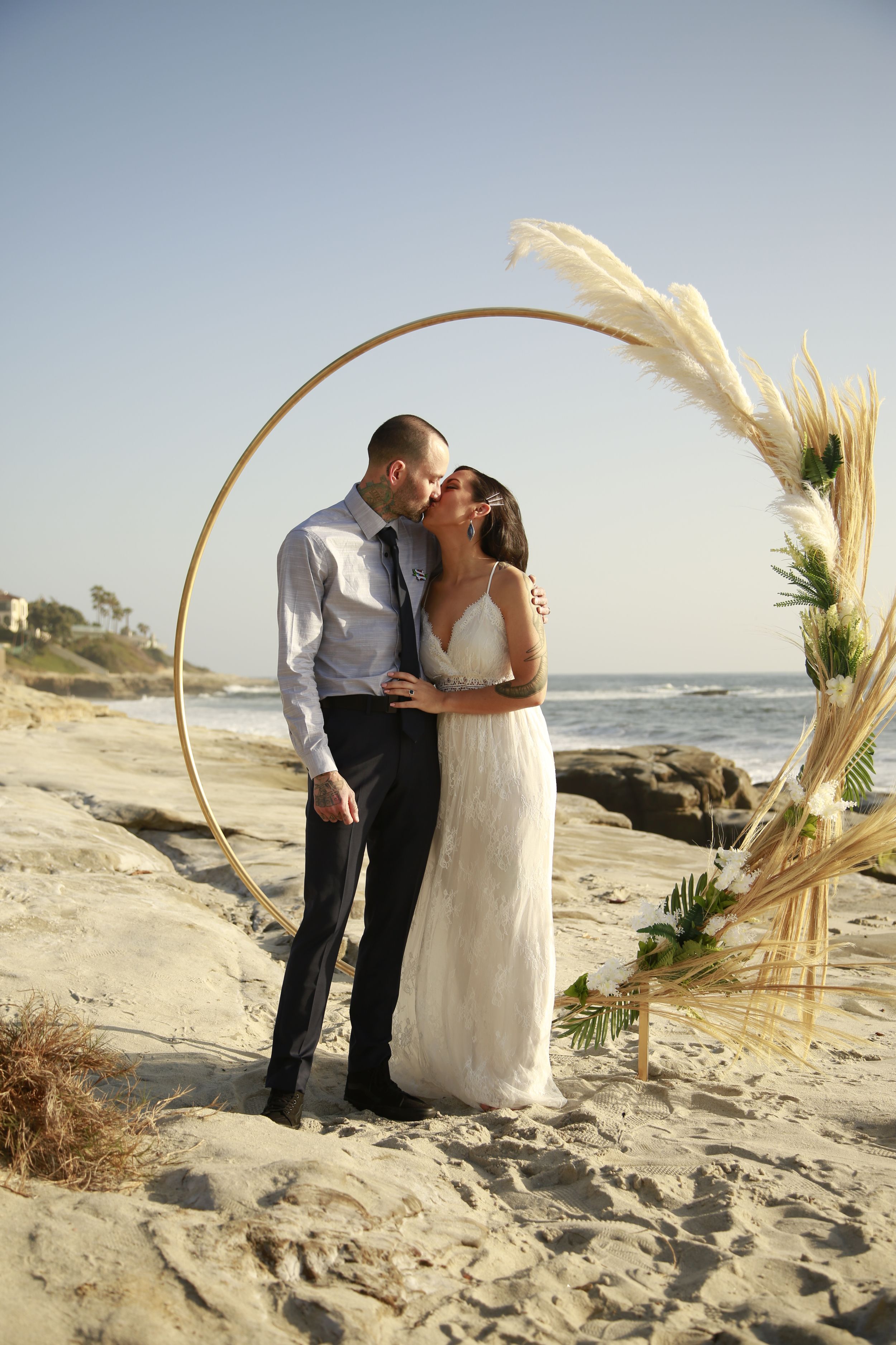 A beach wedding ceremony setup with a golden arch decorated with pampas grass.