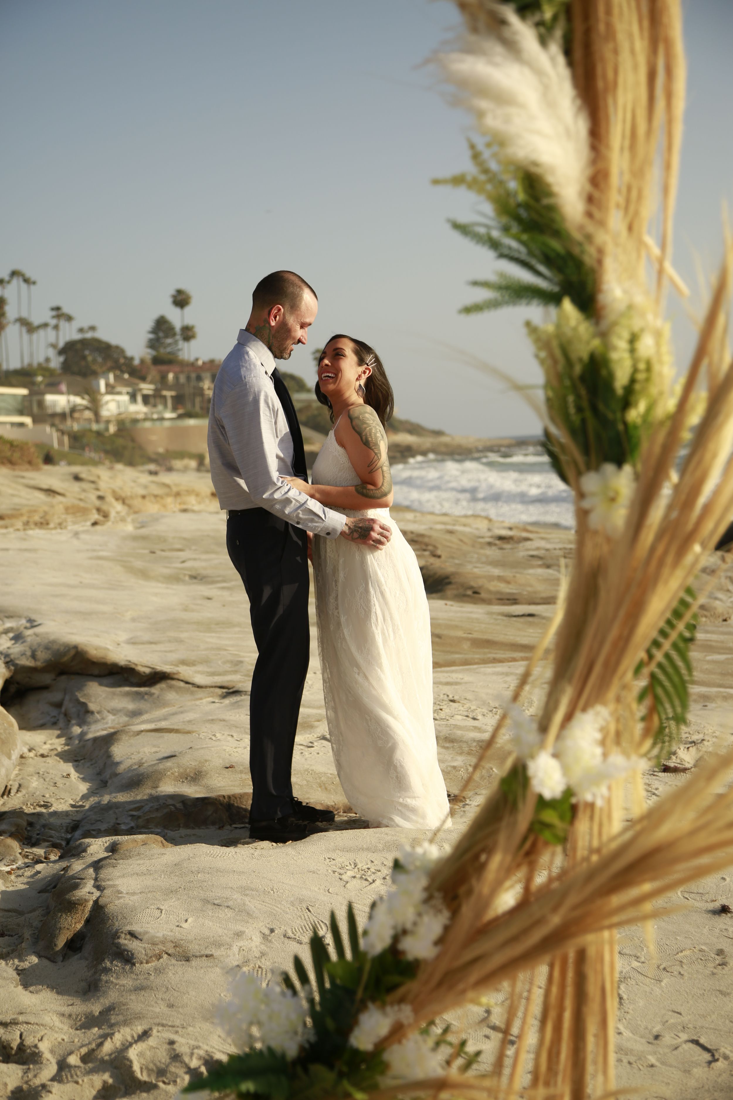 A romantic beach wedding photo with pampas grass decor in the foreground.