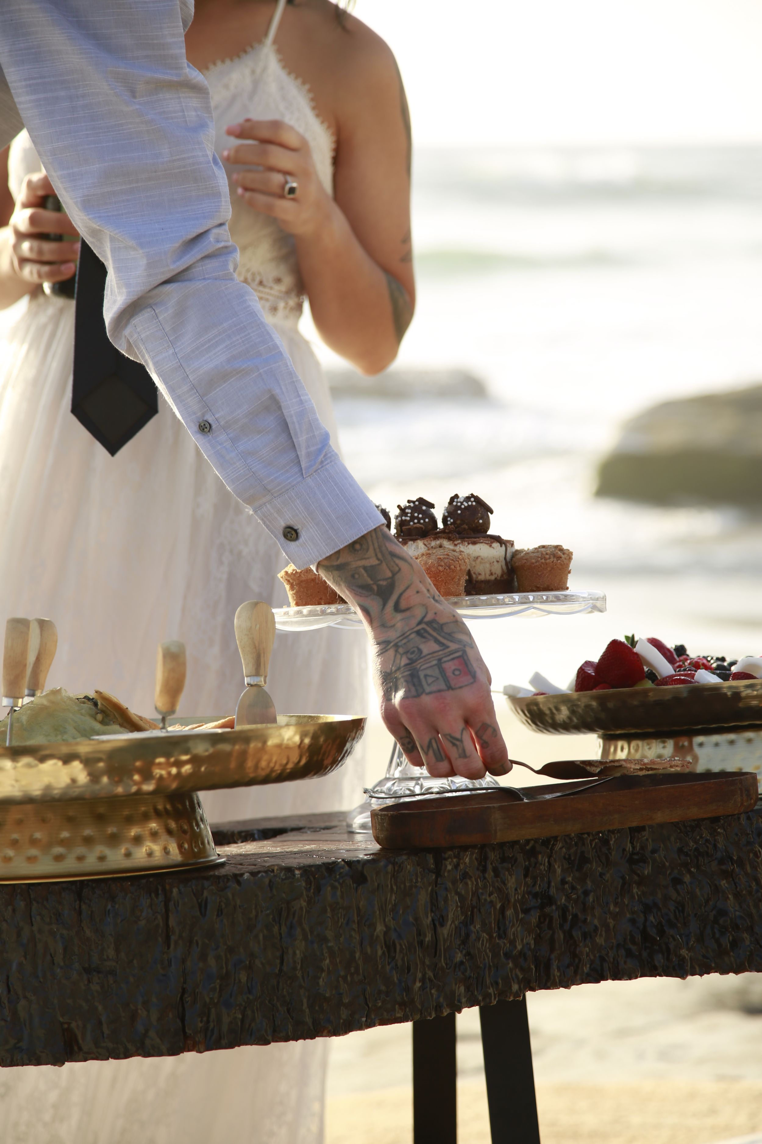 Close-up of desserts and treats on a rustic table at a beach wedding.