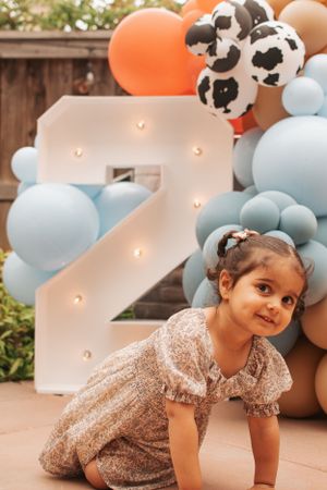 Child in sequined dress plays near balloon decorations and illuminated number display.